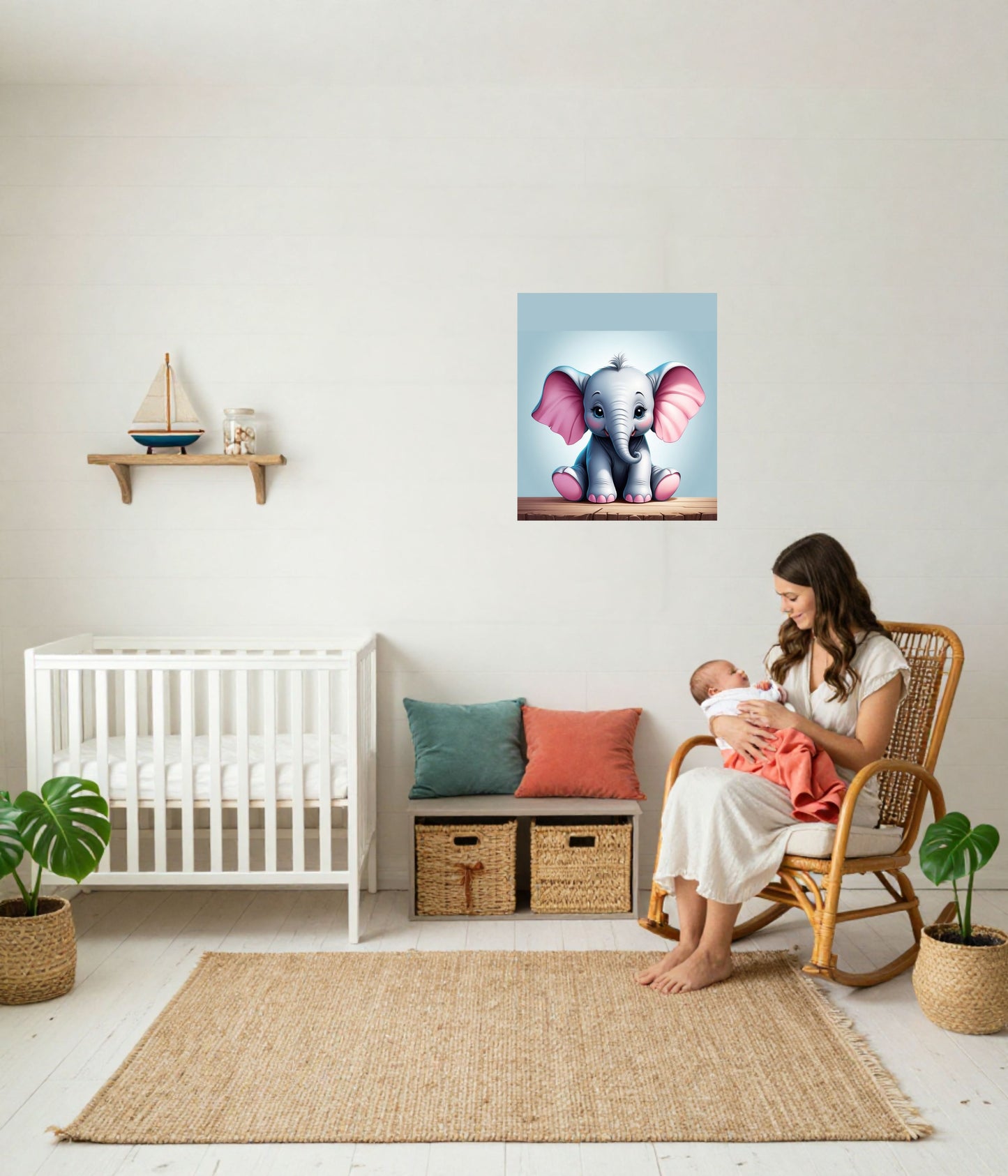 A framed wall art print of a cute baby elephant with pink ears on a light blue background, displayed in a styled nursery above a white crib and next to a woman sitting in a wicker rocking chair with a baby.