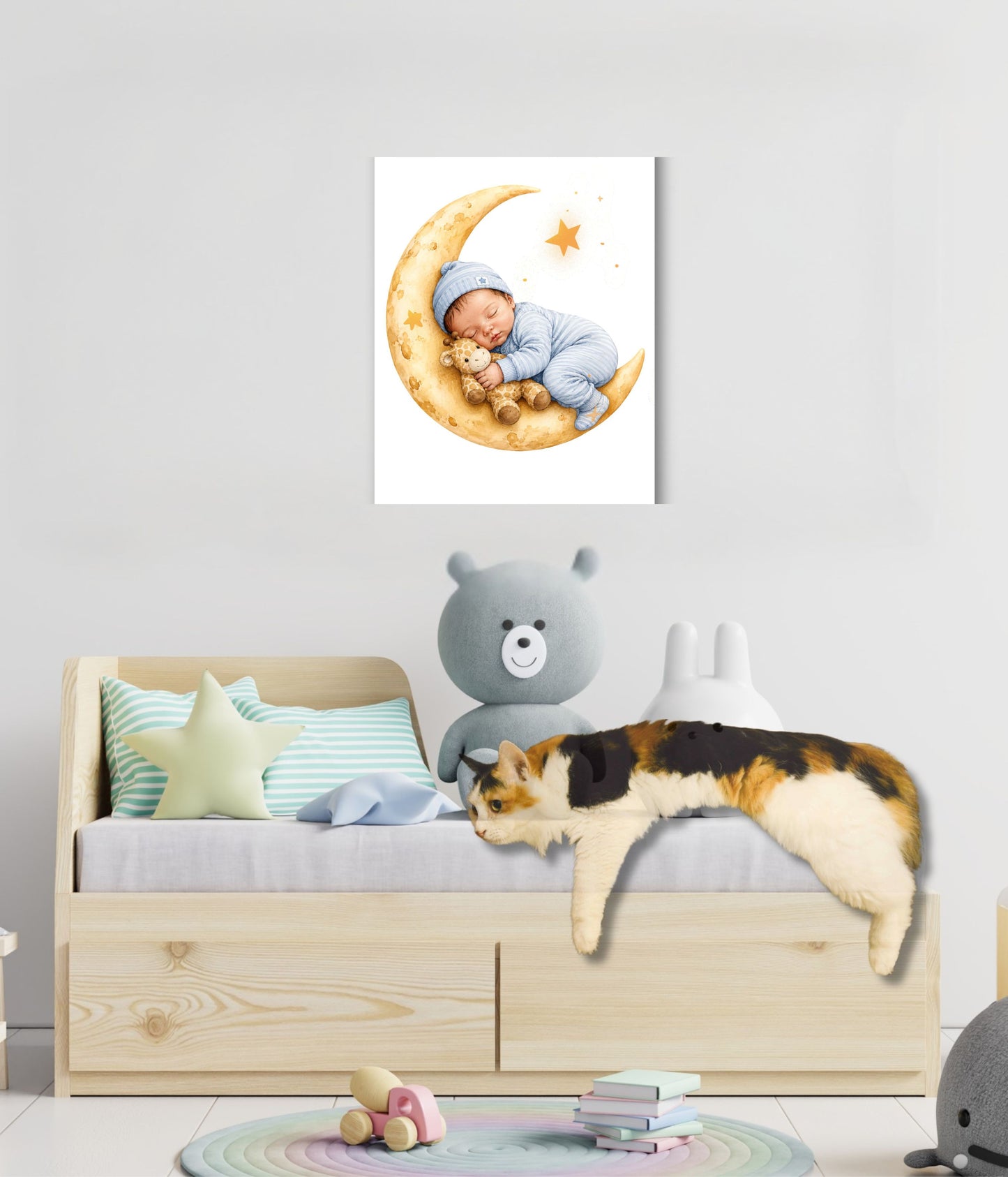 A wall-mounted canvas print showing a sleeping baby on a crescent moon, displayed above a children's bed in a styled nursery. The room includes a wooden bed frame, pastel pillows, a gray teddy bear, and a calico cat lying on the bed.