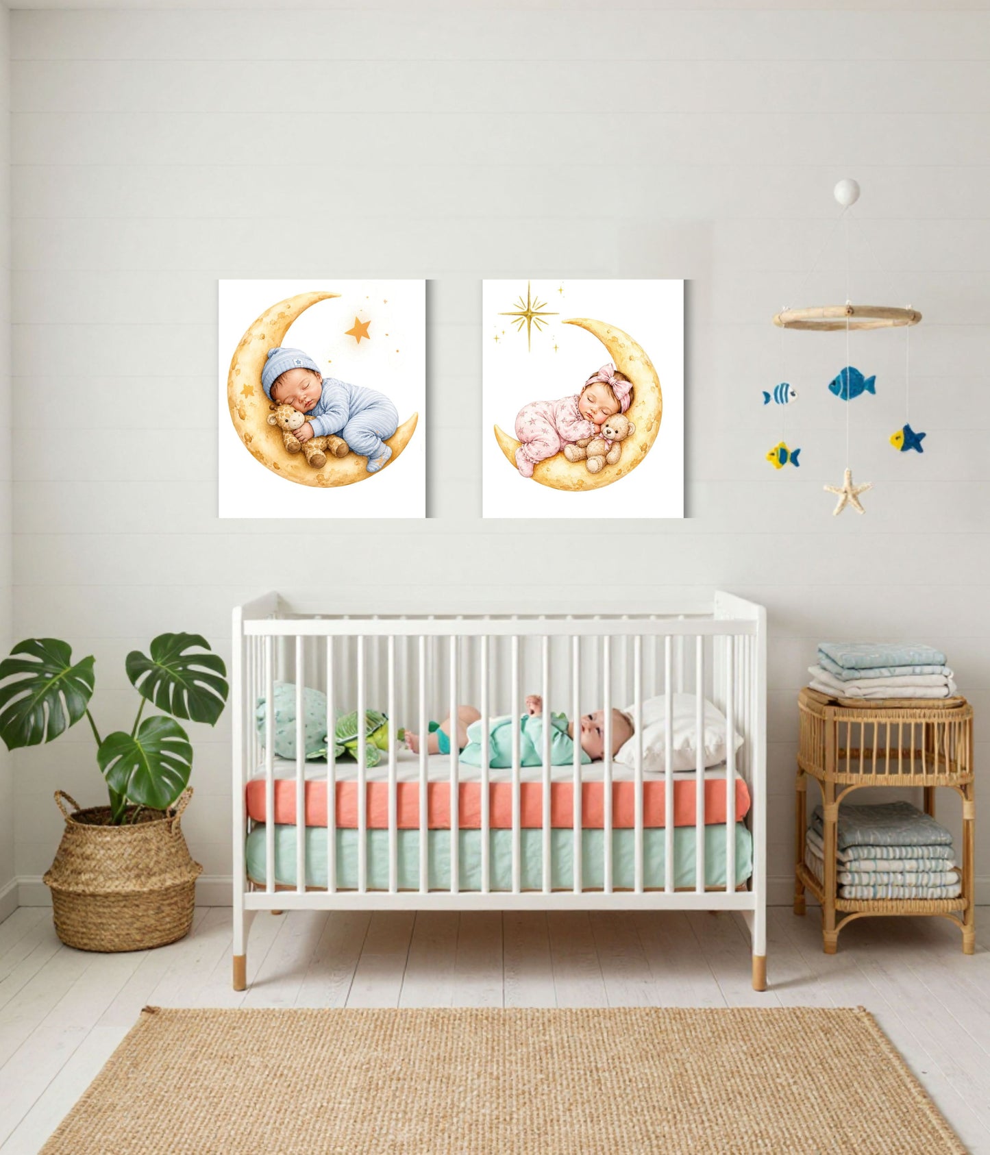 A styled nursery interior with two framed watercolor prints above a white crib. The prints show a baby sleeping on a crescent moon with stars.