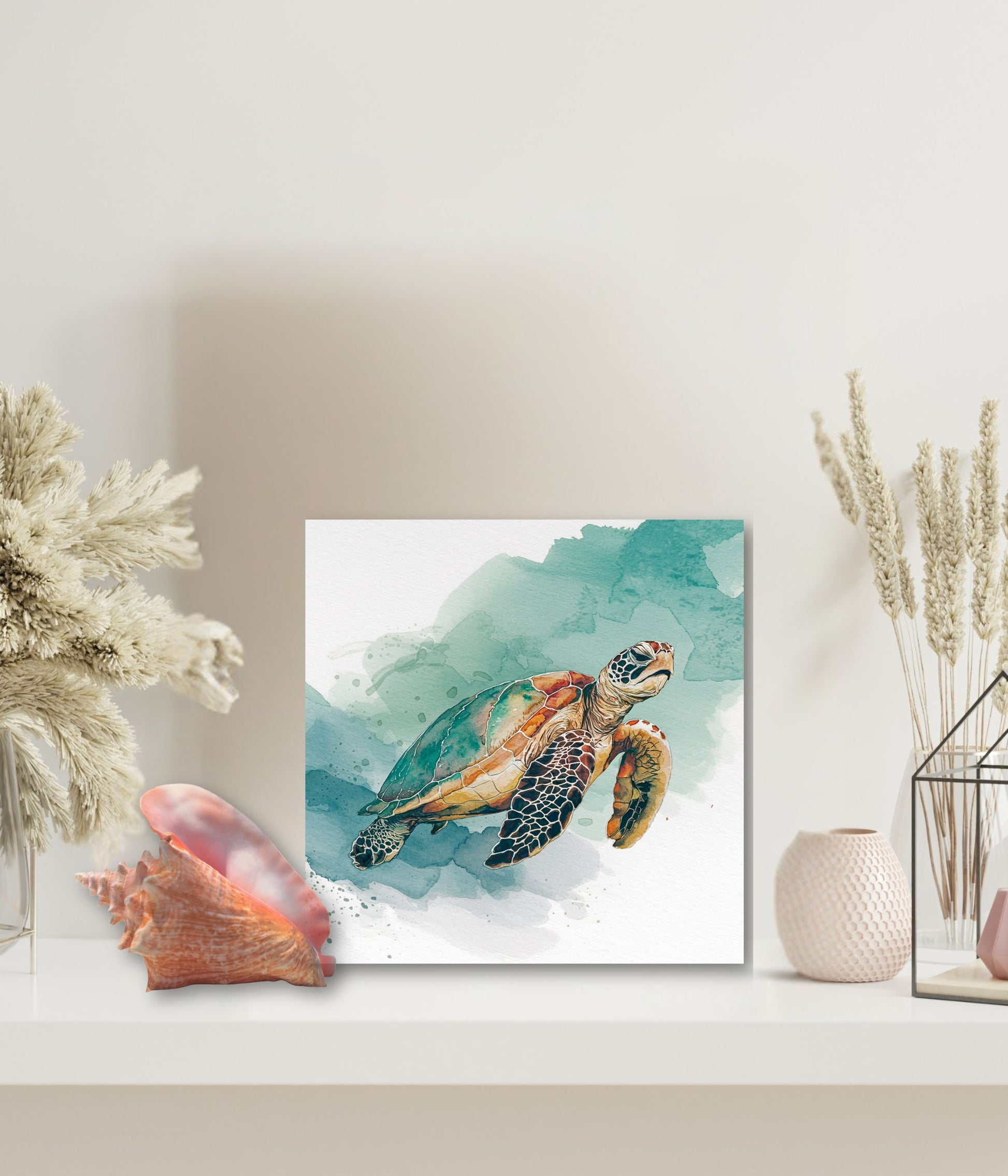 A square wall art print featuring a painted sea turtle over teal and white watercolor washes, displayed on a white shelf with dried plants, a pink shell, and a small vase.