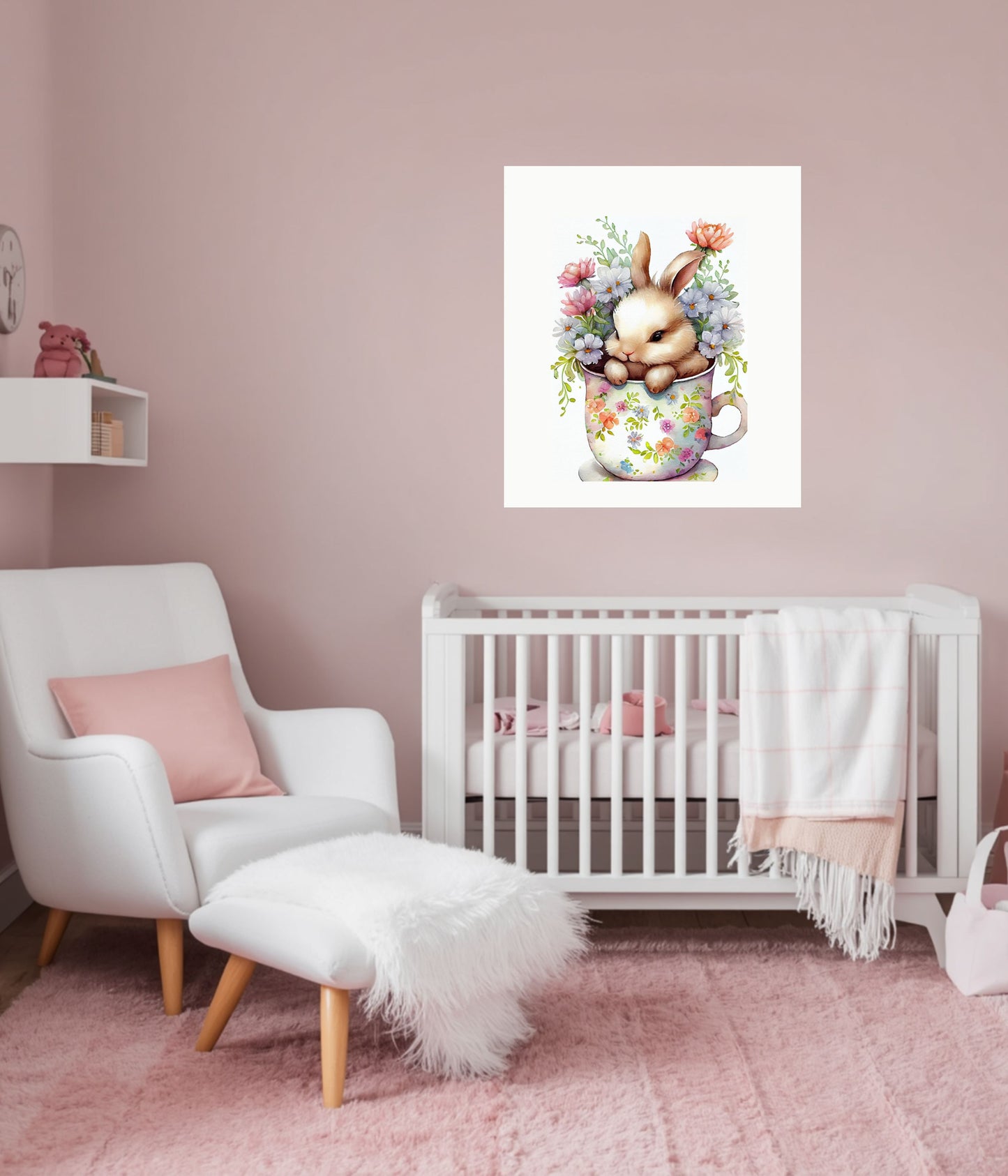 A nursery room scene with a white crib, white armchair, pink rug, and a framed wall art print above the crib showing a sleeping bunny in a floral teacup mug.