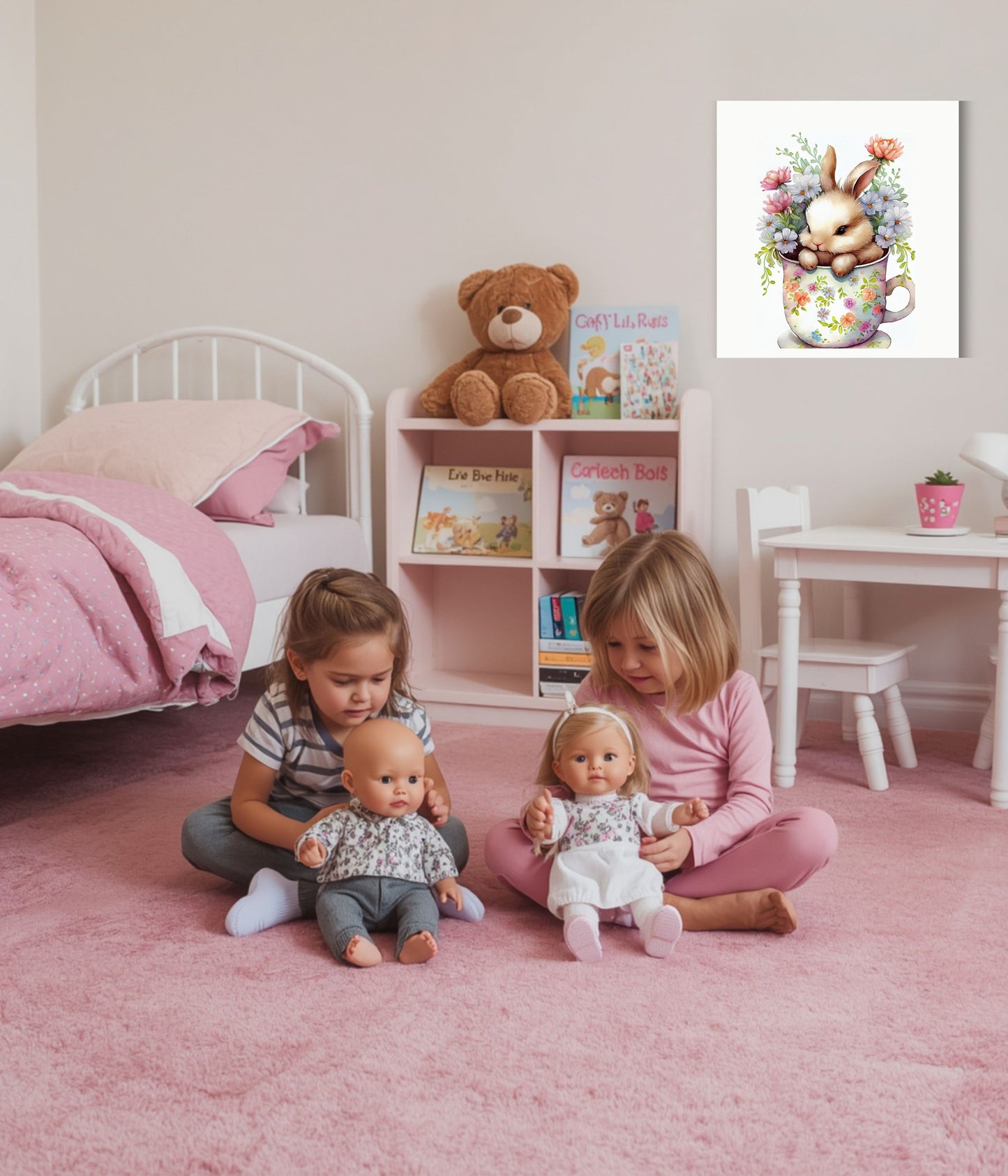 A framed art print featuring a cute bunny bouquet in a floral teacup is displayed on a light pink wall in a children's bedroom. Two young girls are sitting on a pink carpet, playing with baby dolls, with a pink bed, toy shelf, and white table in the background.